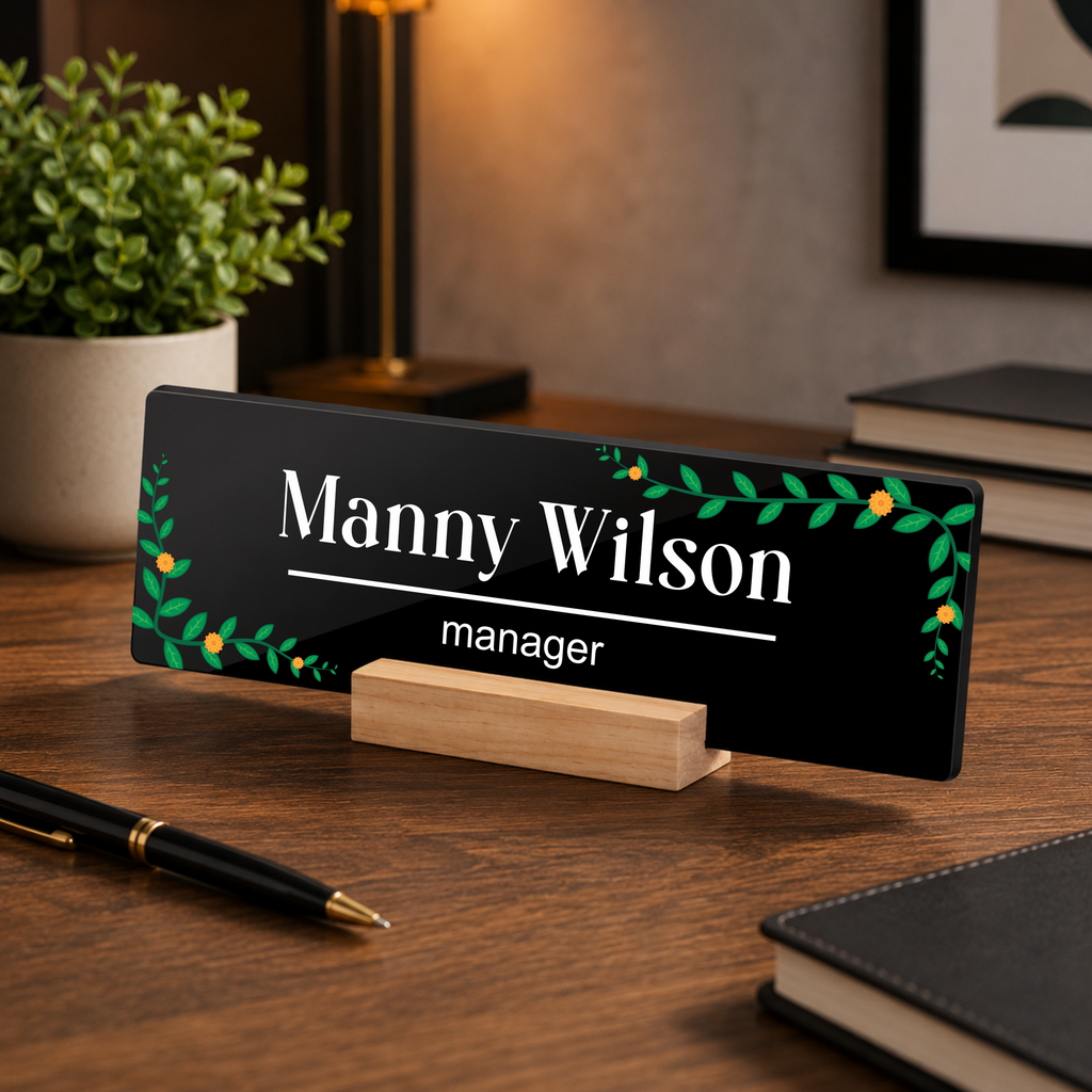 Black acrylic desk name plate with Manny Wilson text, green floral border, wood stand