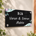 Black acrylic door name plate with floral corners, B-24 and Varun & Simran Mehta.