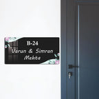 Wall-mounted black acrylic door name plate with floral corners, B-24 and Varun & Simran Mehta.