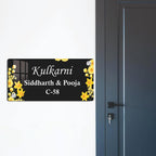Black acrylic door name plate with yellow flower border, mounted on a dark door