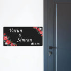 Black acrylic door name plate with floral corners and engraved text, Varun & Simran