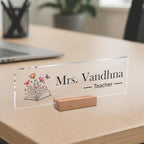 Transparent acrylic desk name plate with Mrs. Vandhna, Teacher text and open-book floral art.