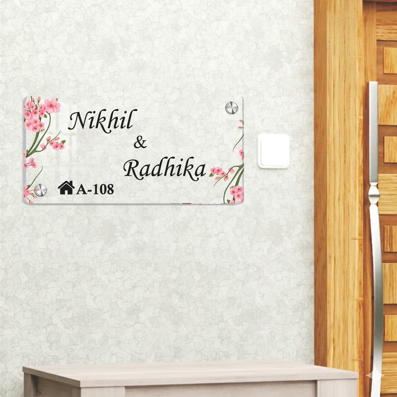 Transparent acrylic door name plate with cherry blossom design: Nikhil & Radhika, A-108, on wall.