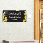 Black acrylic door name plate with yellow flower border on textured wall