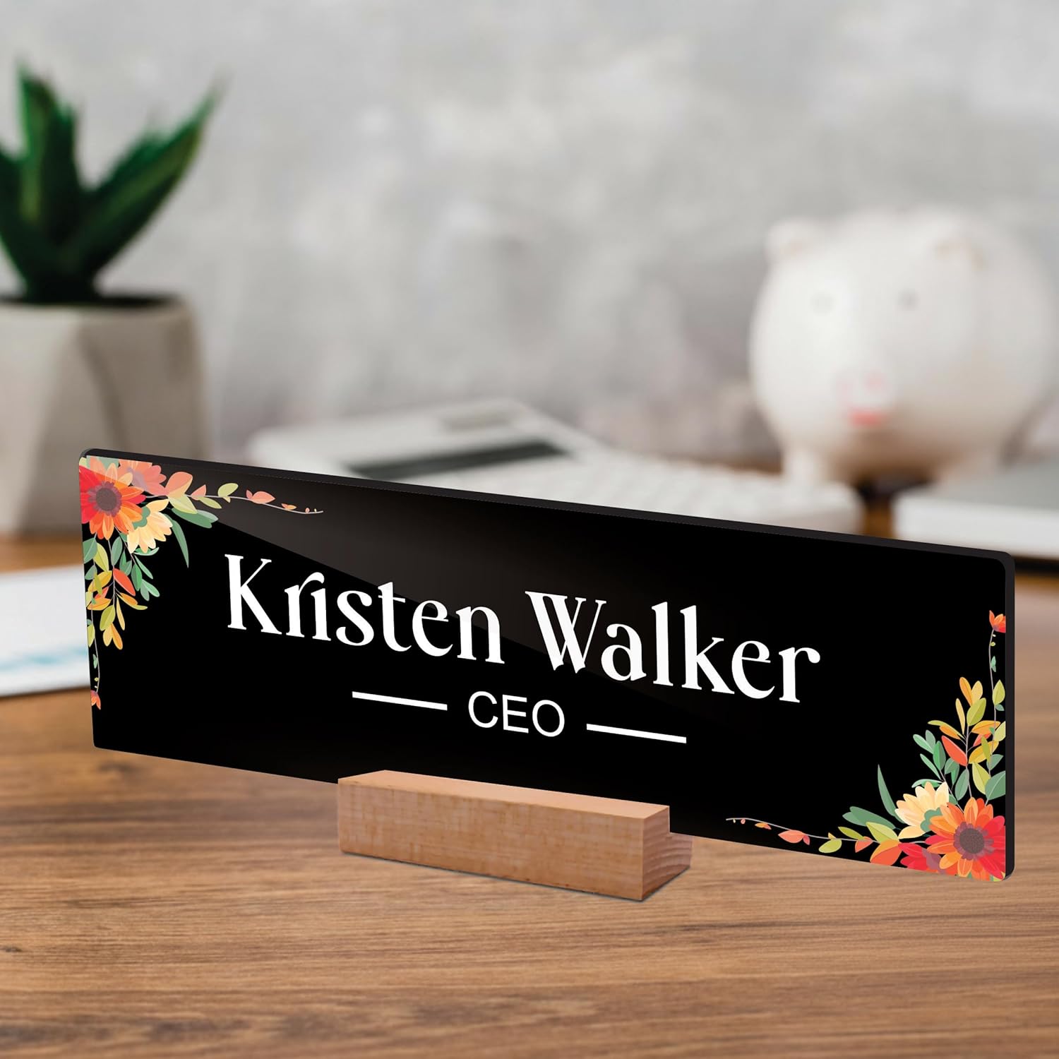 Black acrylic desk name plate with floral border, 'Kristen Walker' and CEO on wooden stand