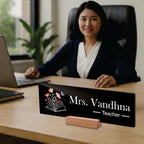Black acrylic desk name plate reading Mrs. Vandhna Teacher with floral book icon on wooden stand