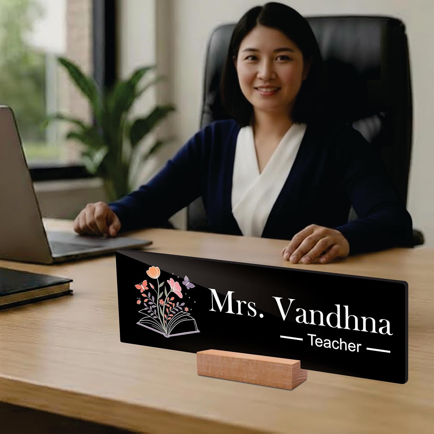 Black acrylic desk name plate reading Mrs. Vandhna Teacher with floral book icon on wooden stand