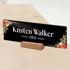 Black acrylic desk name plate with floral border, 'Kristen Walker' and CEO on wooden stand