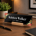 Black acrylic desk name plate with floral border, 'Kristen Walker' and CEO on wooden stand