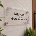 Transparent acrylic name plate with floral corners and engraved “Nilayam Anita & Suresh”